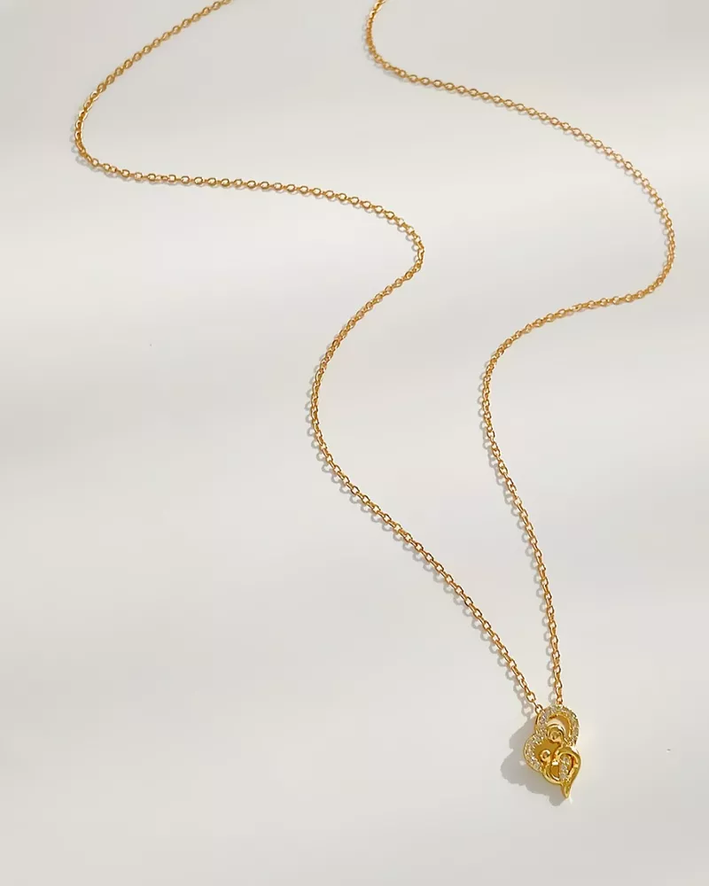 Gold necklace with a heart-shaped pendant on a light gray background