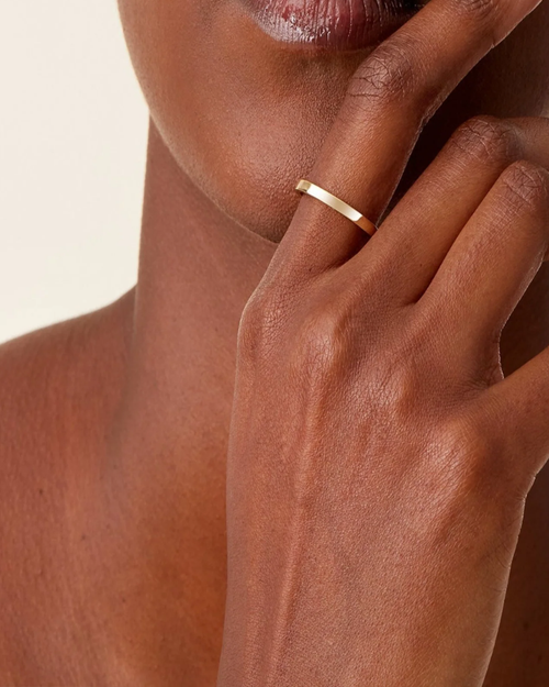 Gold ring on a person's finger against a neutral background
