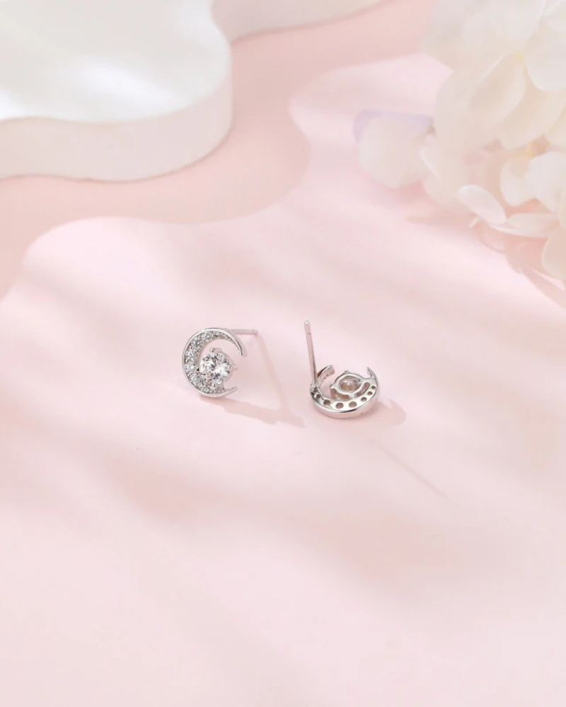 Pair of silver earrings with clear gemstones on a soft pink fabric background