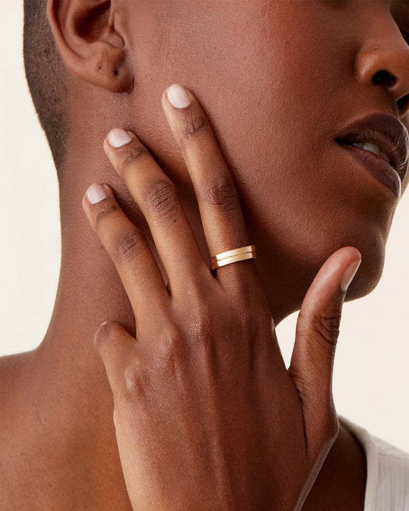 Close-up of a person wearing a gold ring on a neutral background