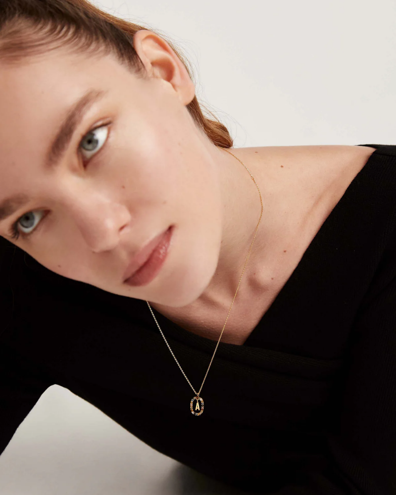 Woman wearing a gold necklace with a pendant against a neutral background