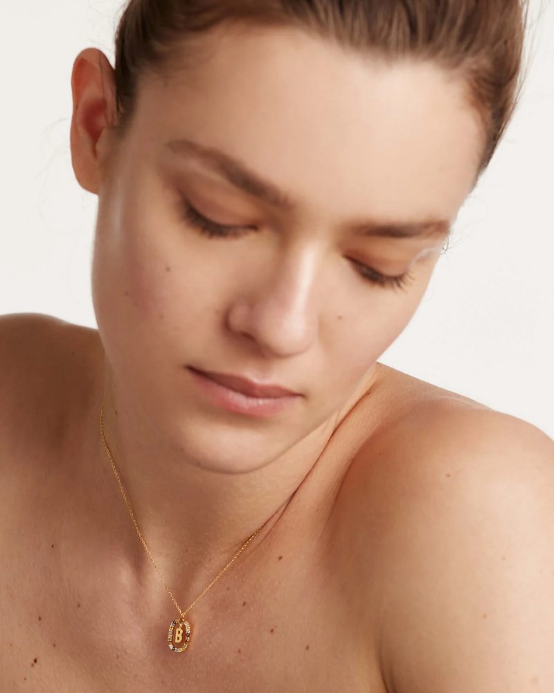 Woman wearing a gold necklace with a 'B' pendant on a white background