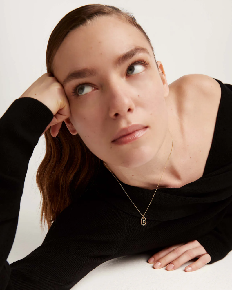 Woman wearing a black top and gold necklace against a white background