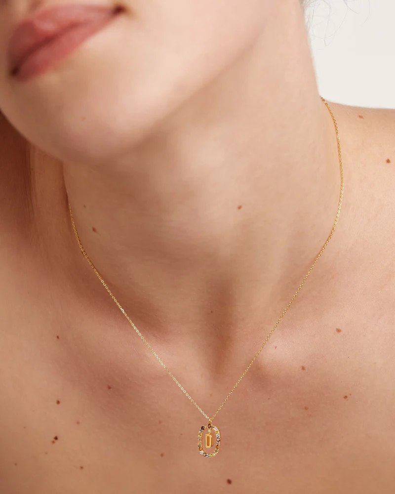 Gold necklace with a pendant on a person's neck against a neutral background