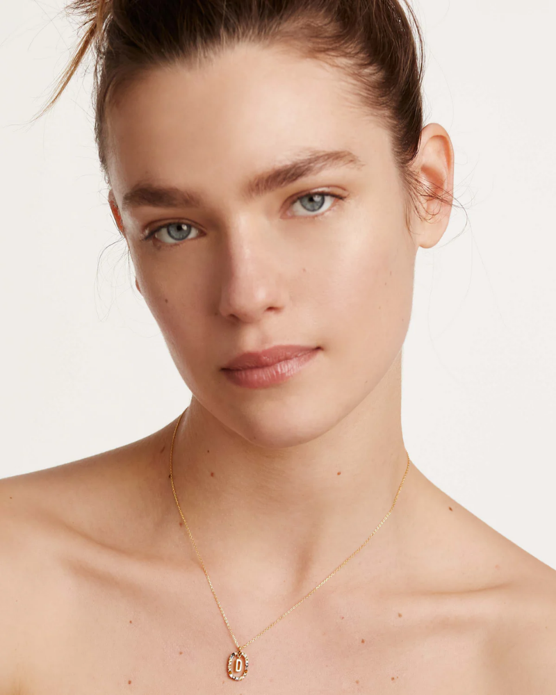 Woman wearing a gold necklace with a pendant on a plain background