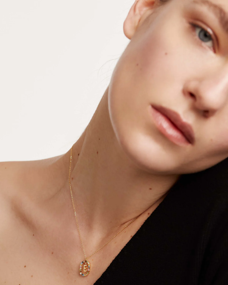 Close-up of a person wearing a gold necklace with a pendant on a plain background