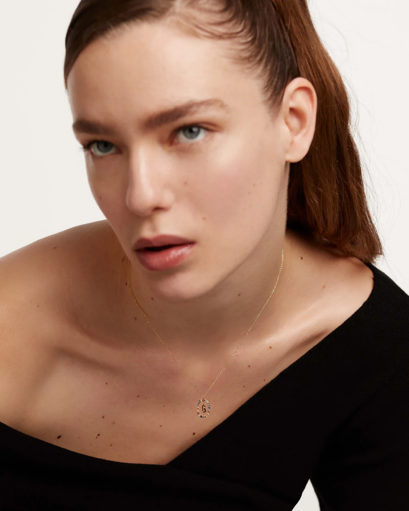 Woman wearing a delicate gold necklace with a small pendant against a neutral background
