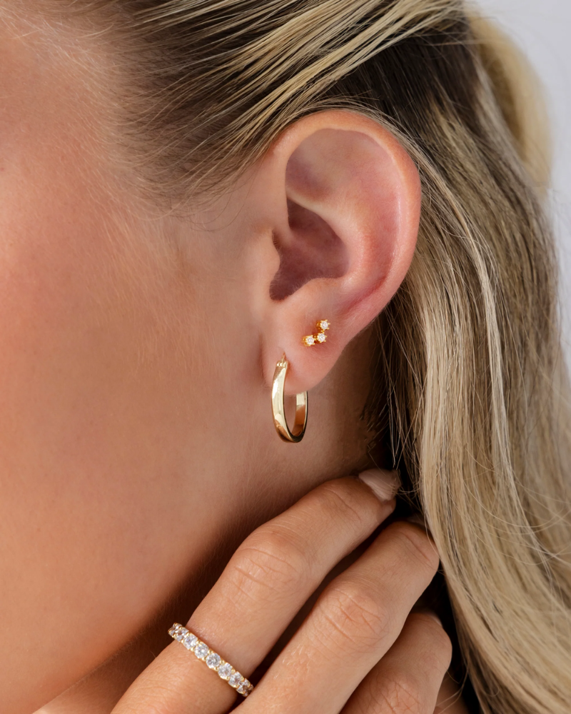 Close-up of a person wearing gold hoop earrings with a blurred background