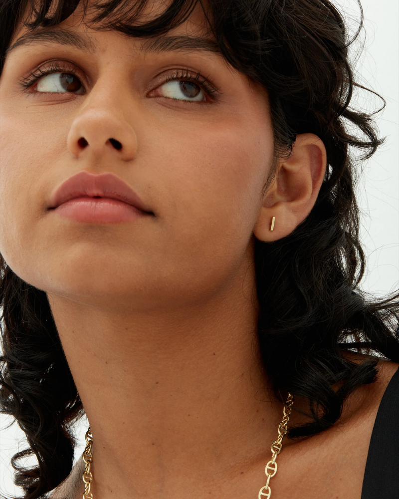 Close-up of a woman wearing gold earrings and a necklace against a neutral background