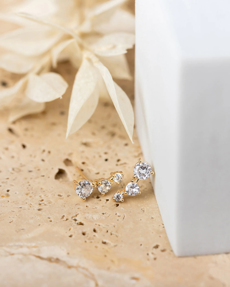 Gold earring with clear stones on a beige surface