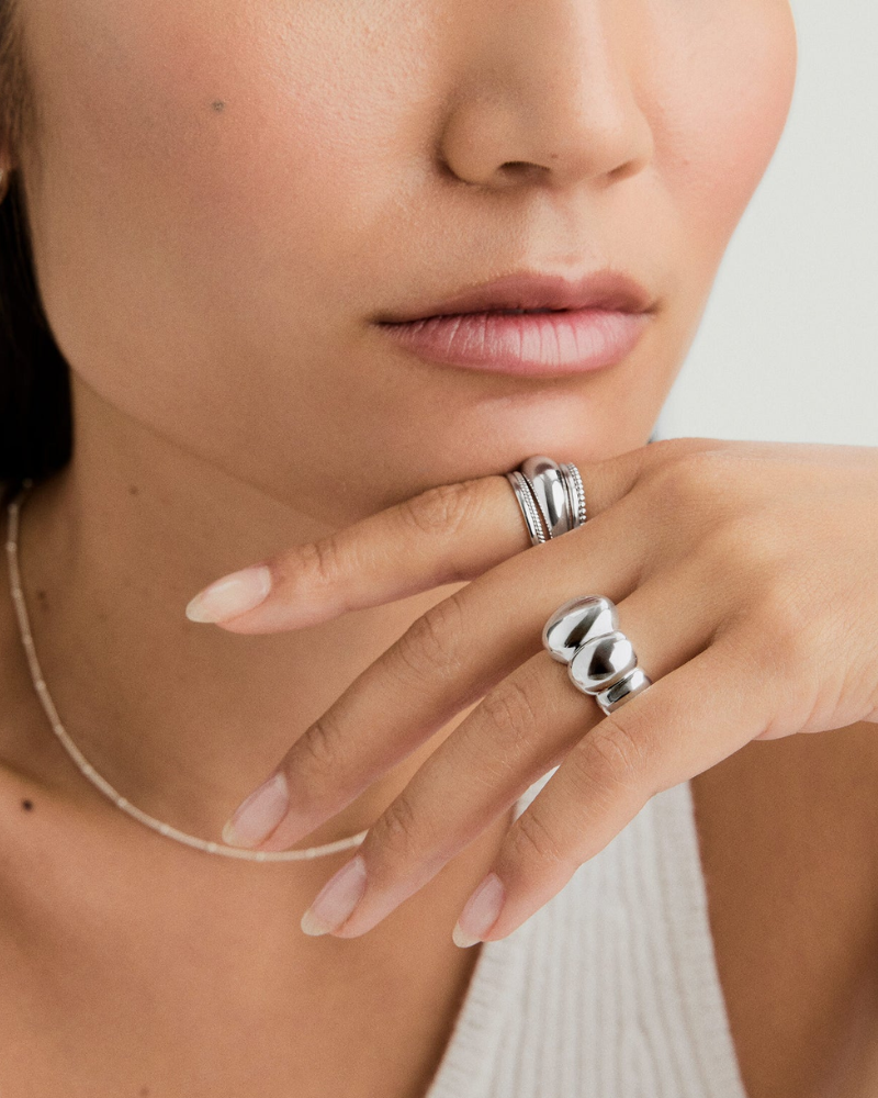 Close-up of a person's hand wearing two silver rings with a neutral background