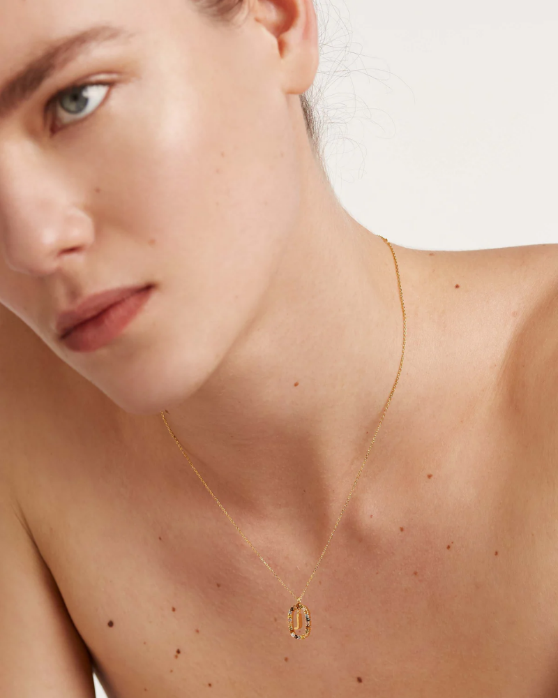 Close-up of a person wearing a gold necklace with a pendant on a plain background