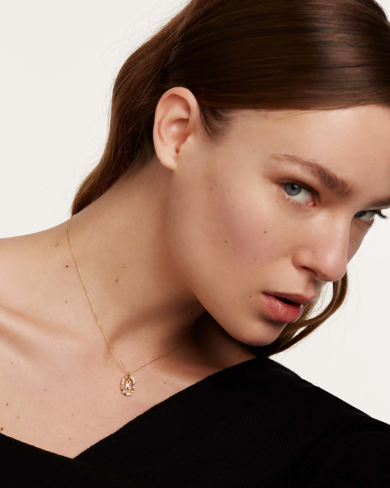 Close-up of a woman wearing a gold necklace with a pendant on a plain background