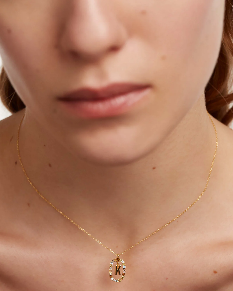Close-up of a person wearing a gold necklace with a 'K' pendant.