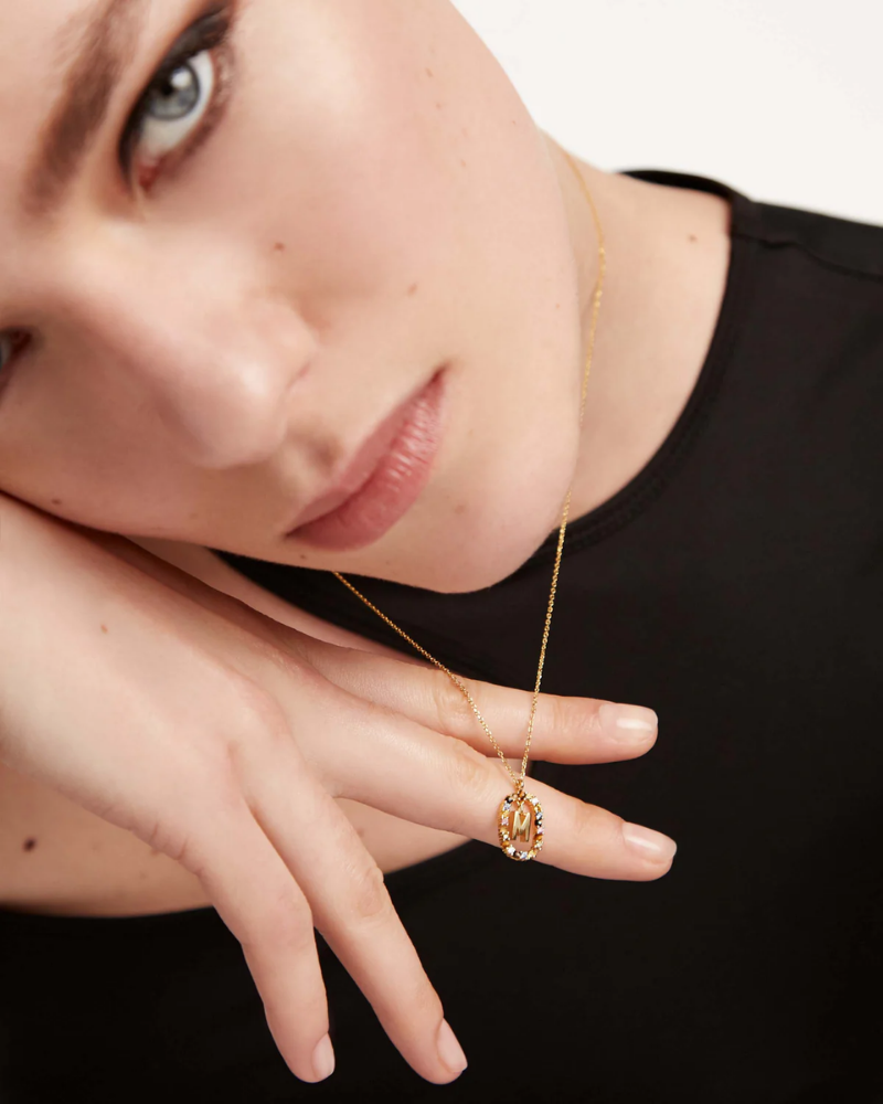 Close-up of a woman wearing a gold necklace and ring on a black background