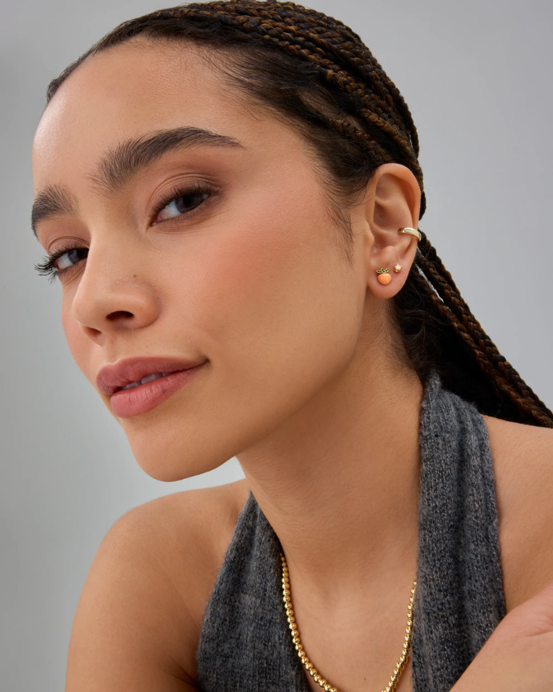 Woman wearing gold earrings and a necklace against a gray background
