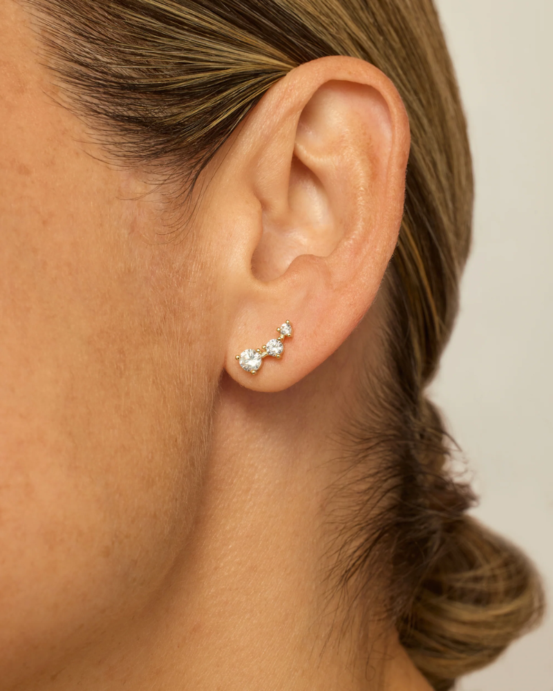 Close-up of an ear wearing a three-stone diamond earring with a neutral background