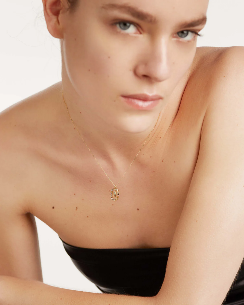Woman wearing a gold necklace with a small pendant on a plain background