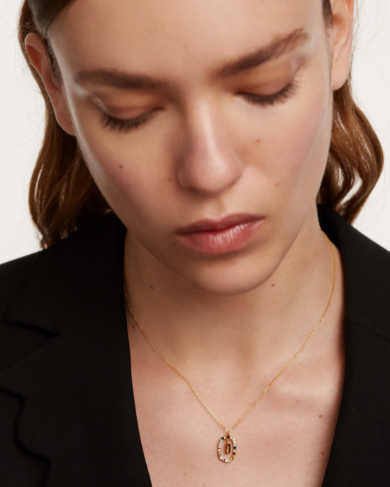 Woman wearing a gold necklace with a pendant on a plain background