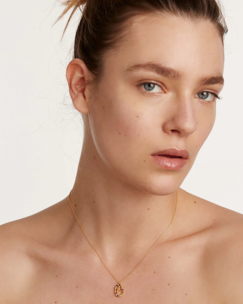 Close-up of a person wearing a gold necklace with a pendant on a plain background