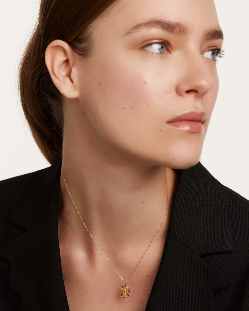Close-up of a woman wearing a gold necklace with a pendant against a neutral background