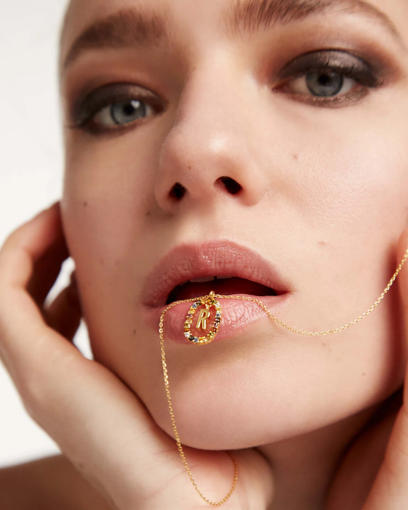 Close-up of a woman's face with a gold necklace and ring on a white background