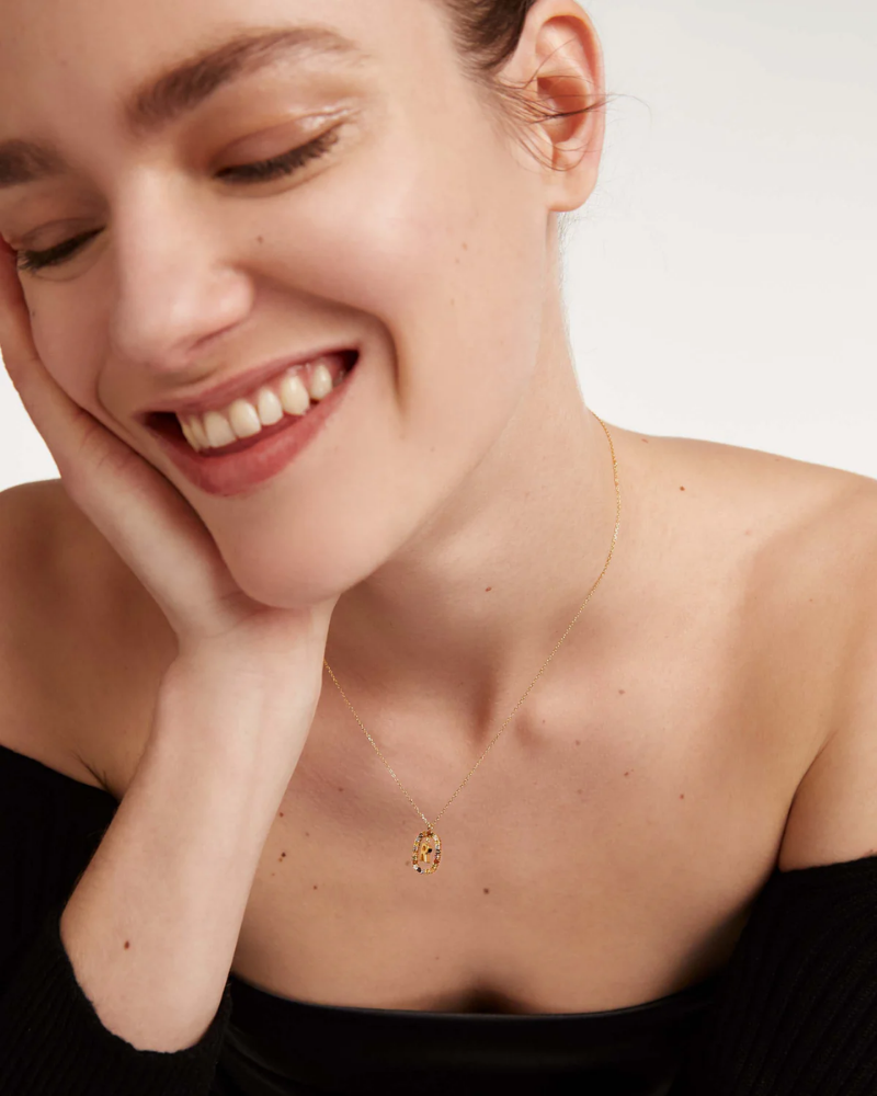 Woman wearing a delicate gold necklace with a small pendant on a plain background
