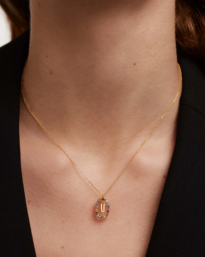 Gold necklace with a pendant on a person's neck against a black background