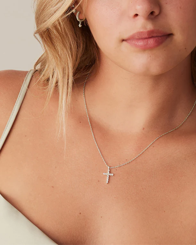 Close-up of a woman wearing a silver cross necklace against a neutral background
