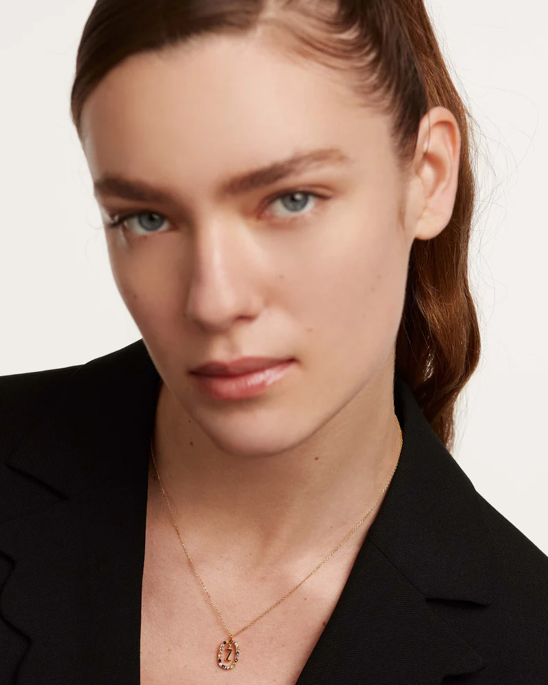 Close-up of a person wearing a black blazer and gold necklace on a white background